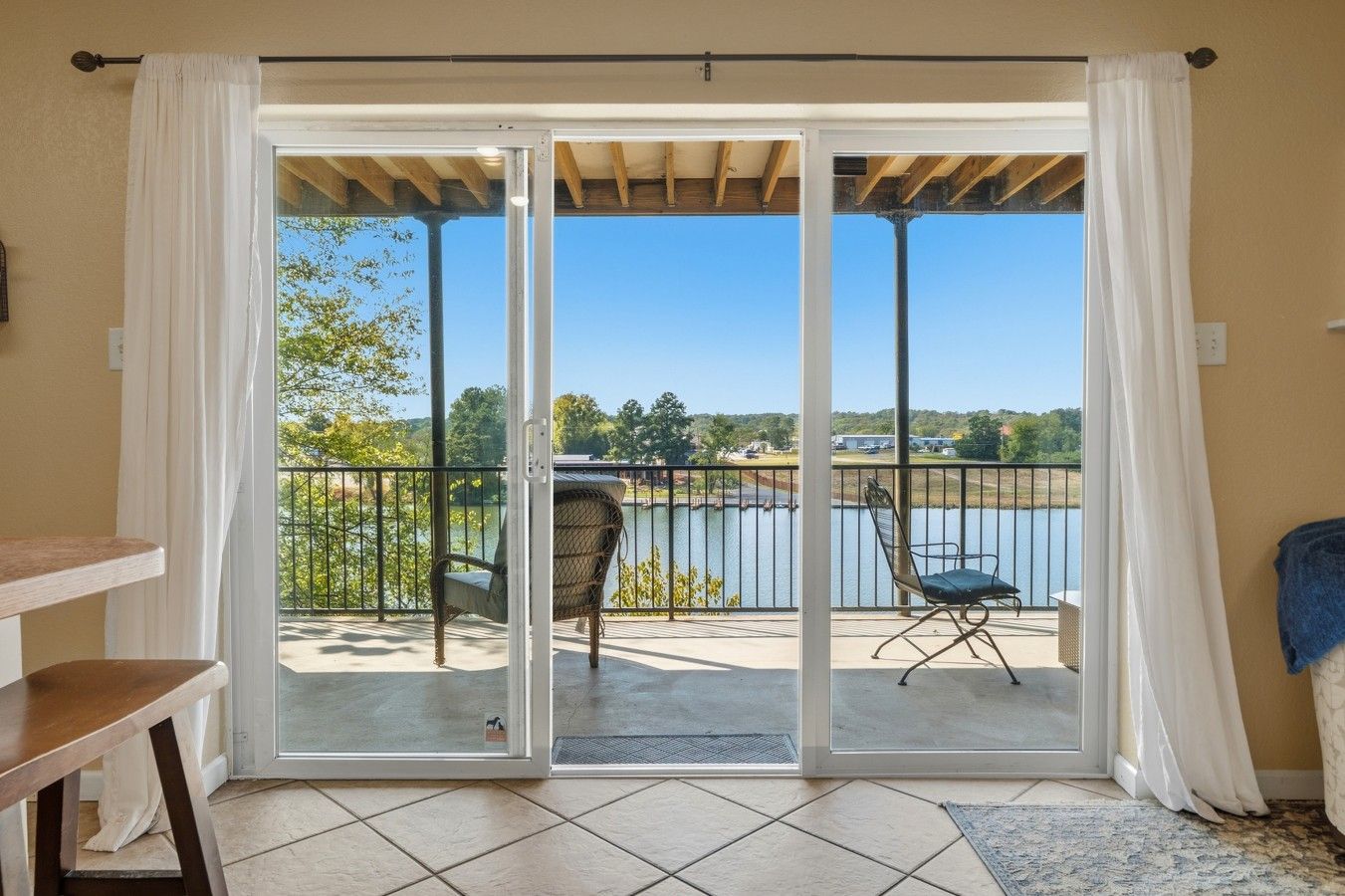Une pièce dotée d’une porte-fenêtre coulissante donnant sur un balcon avec deux chaises et une vue sur un lac.