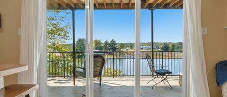 Une pièce dotée d’une porte-fenêtre coulissante donnant sur un balcon avec deux chaises et une vue sur un lac.