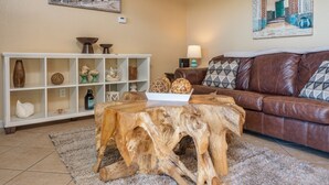A living room with a brown leather sofa, a white shelving unit with decorative items, and a wooden coffee table.