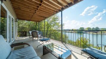 Ein überdachter Außenbereich mit Blick auf einen See, ausgestattet mit einer Couch, Sesseln und einem Tisch.