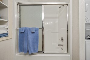 Une salle de bain avec une porte de douche, un porte-serviettes avec des serviettes pliées et un mur blanc.