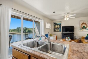 Una cocina con un lavaplatos doble, un ventilador de techo, un televisor y vistas a un lago.