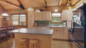 A cabin-style kitchen with wooden beams, a central island with stools, a refrigerator, and a sink. - Bison Acres Close to Crystal Mt with Hot Tub (Beulah)