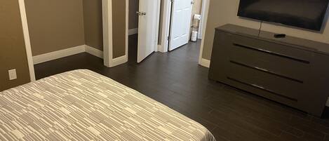 A bedroom with a bed, a dresser, a TV, and a door leading to a bathroom.
