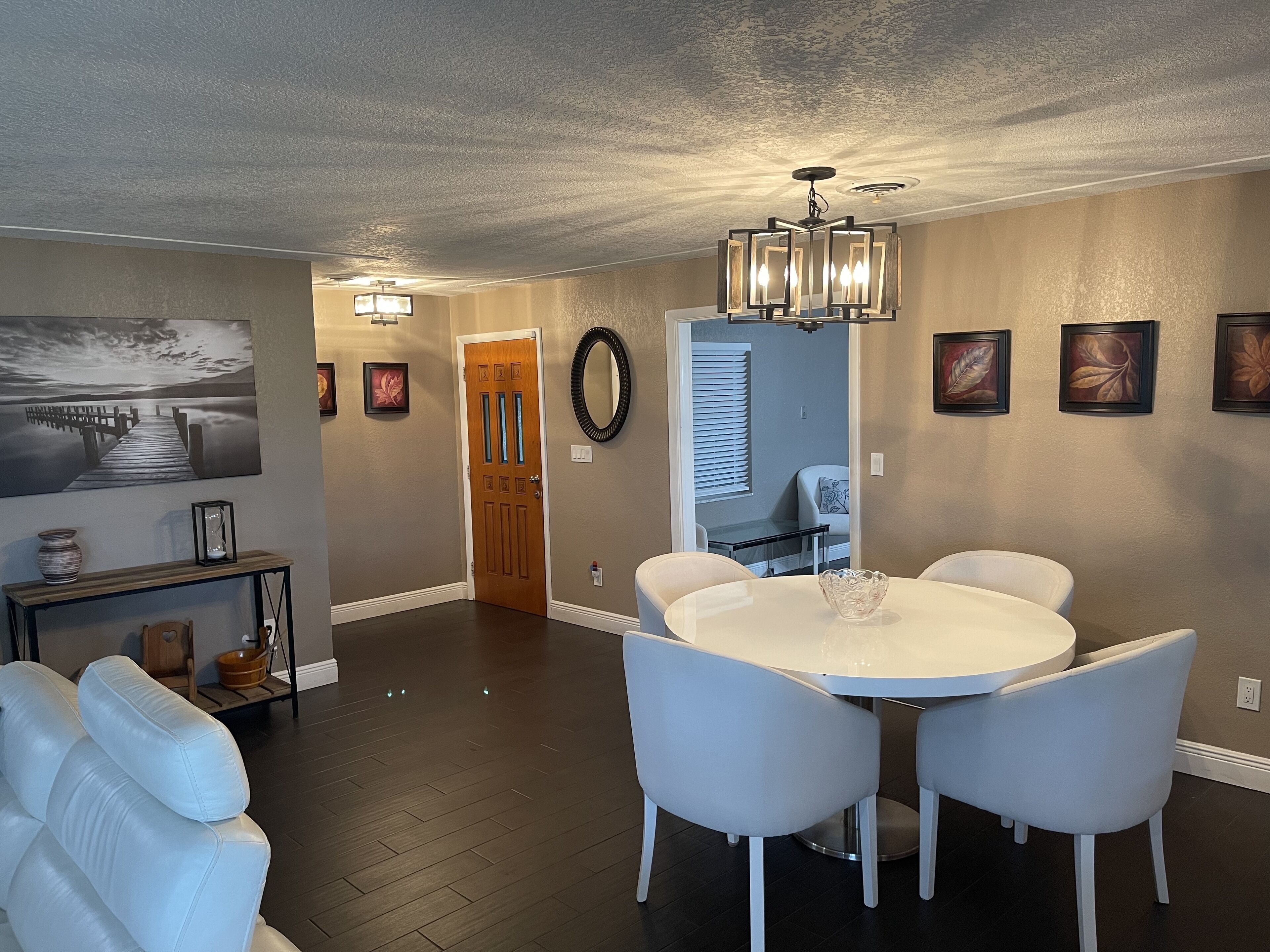 A dining area with a round table and four chairs, a chandelier, and a painting on the wall.