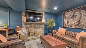 A living room with a stone fireplace, leather sofas, a television mounted above the fireplace, and a large owl painting on the wall. - Tranquil mountainhouse w/hot tub, super close to trails & wineries- pet friendly (Linden)