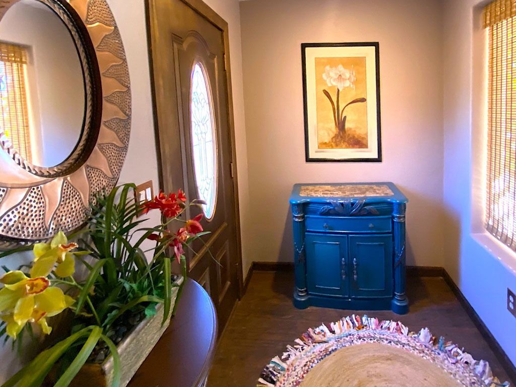 A hallway with a blue cabinet, a framed flower painting, and a mirror with a decorative frame.