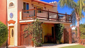 A two-story building with a balcony, a door with a decorative emblem, and a fenced garden area. - Cozy Casita, overlooking Senoran Desert Peserve, Cave Creek (Phoenix)