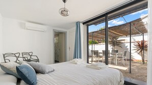 A bedroom with a bed, pillows, a ceiling light, and a view of an outdoor patio with a table and chairs. - WELCS VILLA 022 EMP La Morgana con piscina priva (Empuriabrava)