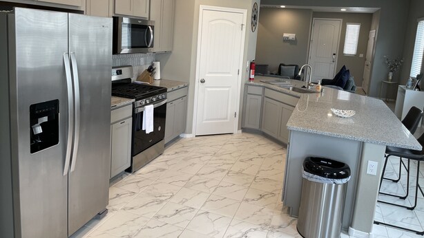 A modern kitchen with stainless steel appliances, a marble-tiled floor, and a central island.