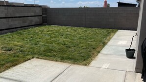 A concrete patio with a grassy area and a brick wall.