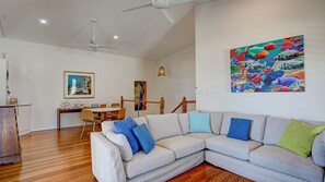 A living room with a sectional sofa, a dining area with a table and chairs, and a colorful mural on the wall.