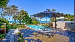 A wooden deck with a pool, lounge chairs, and a view of the ocean.