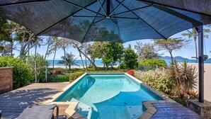 A swimming pool with a view of the ocean, surrounded by tropical vegetation and a covered area with a canopy.