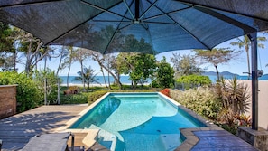 A swimming pool with a view of the ocean, surrounded by tropical vegetation and a covered area with a canopy.