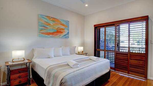 A bedroom with a bed, bedside tables, a painting, and a window with blinds.
