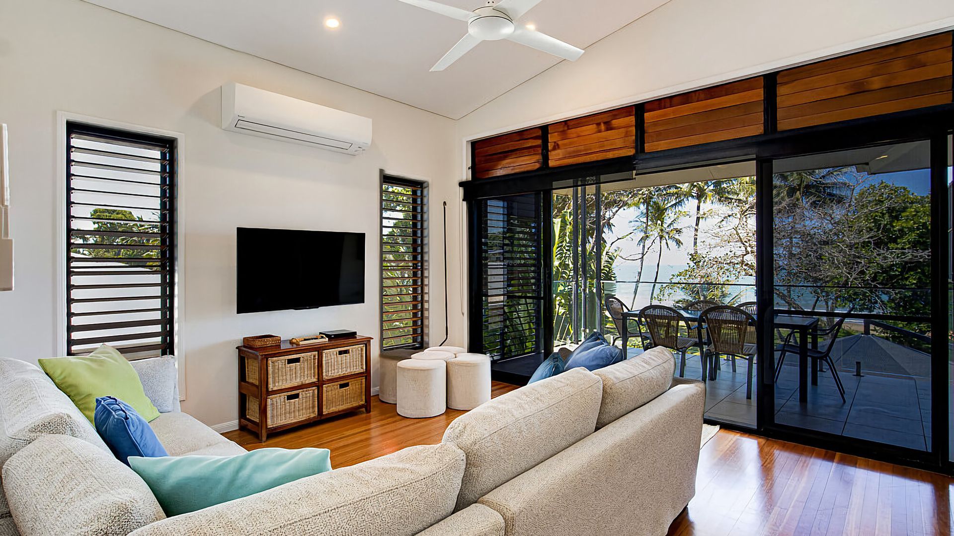 A modern living room with a flat-screen TV, wooden flooring, and a balcony with outdoor furniture.