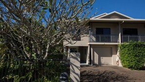 A two-story residential building with a balcony, a garage, and a fenced yard.