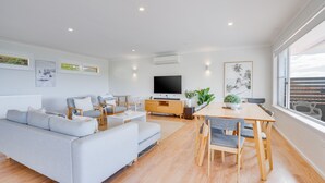 A modern living room with a grey sofa, a dining table with chairs, a flat-screen TV, and artwork on the walls. - Becker Bliss - 5 bedrooms, ocean views, sleeps 16 (Forster)