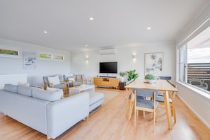 A modern living room with a grey sofa, a dining table with chairs, a flat-screen TV, and artwork on the walls. - Becker Bliss - 5 bedrooms, ocean views, sleeps 16 (Forster)