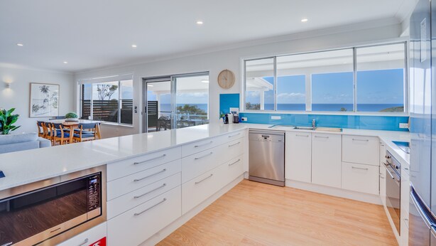 A modern kitchen with white cabinetry, a dishwasher, and a large island. - Becker Bliss - 5 bedrooms, ocean views, sleeps 16 (Forster)