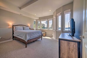 A bedroom with a bed, bedside lamps, a TV on a wooden cabinet, and large windows with a view. - Spacious Lake Stevens Home w/ Fire Pit, Patio (Lake Stevens)