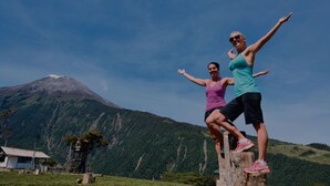 Dos personas de pie sobre un poste de madera, con una montaña al fondo.