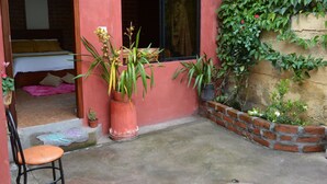 Un pequeño patio con suelo de hormigón, una planta en maceta, una silla y un muro de ladrillo cubierto de plantas trepadoras.