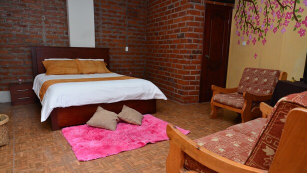 Un dormitorio con pared de ladrillo, cama de madera, una silla y una alfombra rosa.