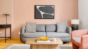Una sala moderna con un sofá grisáceo, cojines estampados, una mesa de centro de madera con libros y una obra de arte abstracta enmarcada en la pared.