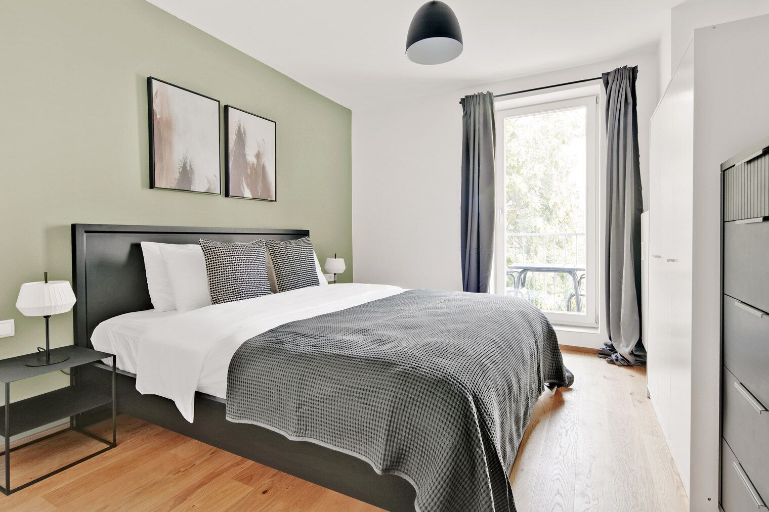 A modern bedroom with a bed, bedside tables, a window with curtains, and artwork on the wall.