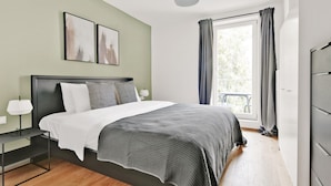 Un dormitorio moderno con cama, mesitas de noche, una ventana con cortinas y una obra de arte en la pared.