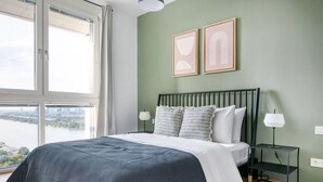 Een slaapkamer met een bed, een nachtkastje, een lamp en twee foto's in lijsten aan de muur.