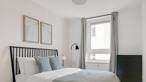 Un dormitorio con cama, mesita de noche, lámpara, ventana con cortinas y cómoda.