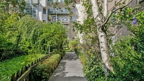 Un sendero estrecho bordeado de exuberante vegetación y un edificio moderno con balcones.