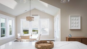 A spacious kitchen with a large island, white cabinetry, and a view of the countryside through large windows. - Waterfront Home with Panoramic Views in Black Dog Harbor, Salvo, NC  (Salvo)