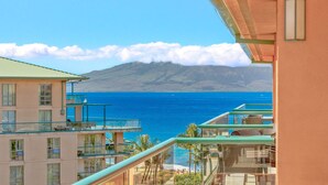 Un hôtel en bord de mer doté de nombreux balcons donnant sur l’océan, avec une montagne en arrière-plan et un ciel dégagé.