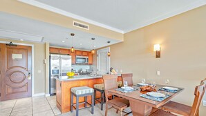 A modern kitchen with a central island, bar stools, and a dining table set for six. - Maui Resort Rentals: Honua Kai - 3BR  Partial Ocean and West Maui Mountain Views! (Lahaina)