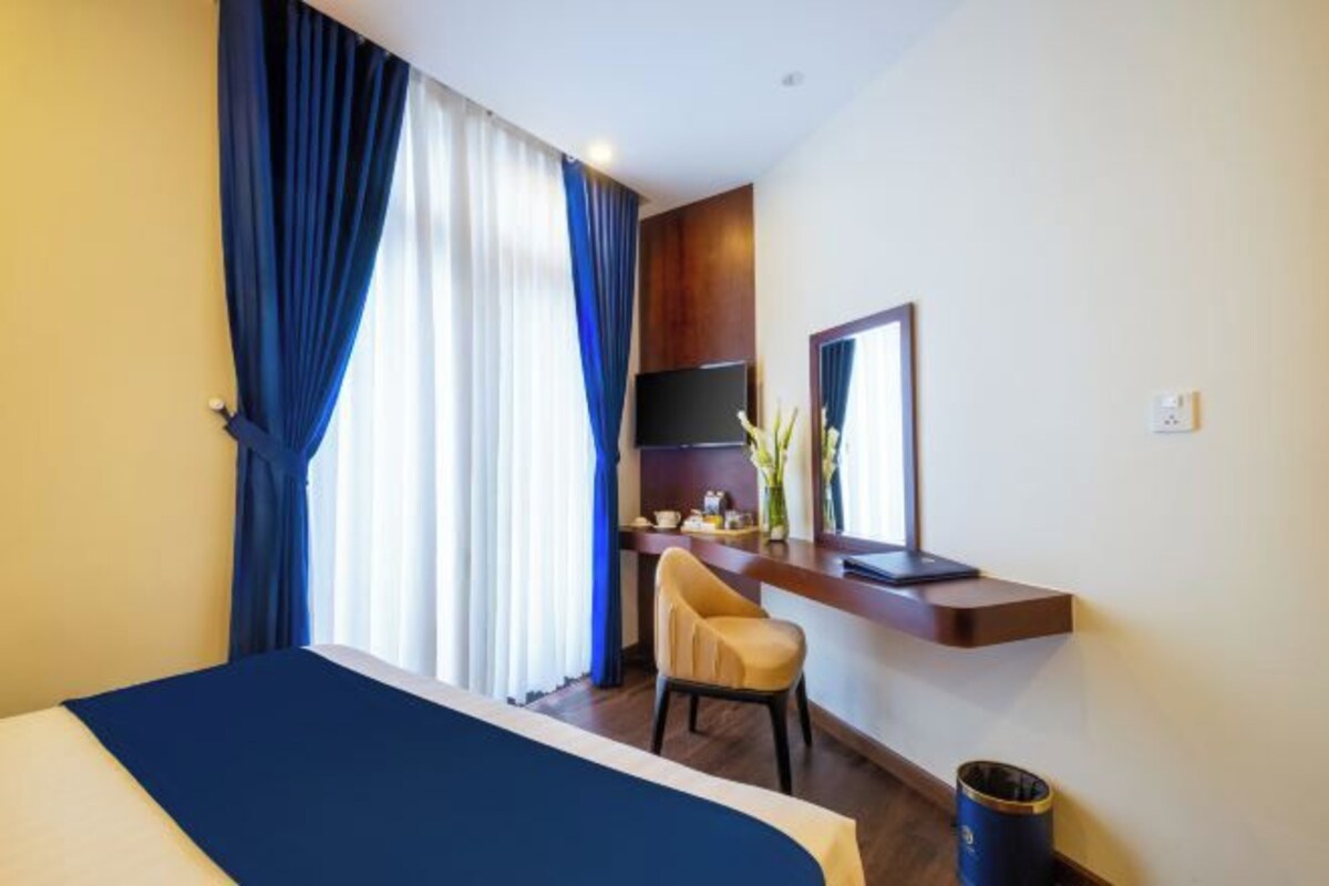 A hotel room with a bed, a desk with a chair, a TV, and a mirror.