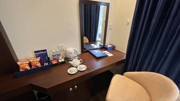 Une chambre d’hôtel avec un bureau en bois, un miroir, une chaise et une petite poubelle.