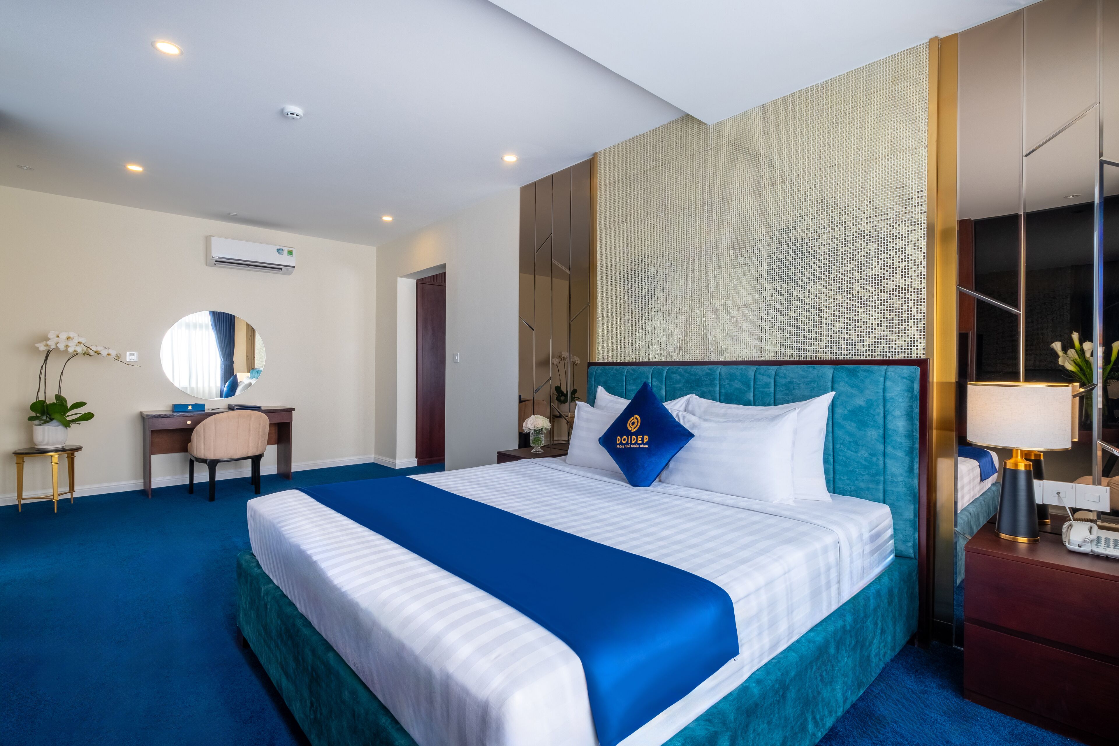 Habitación de hotel con una cama grande, un escritorio, una silla, un espejo y una mesita de noche con una lámpara.