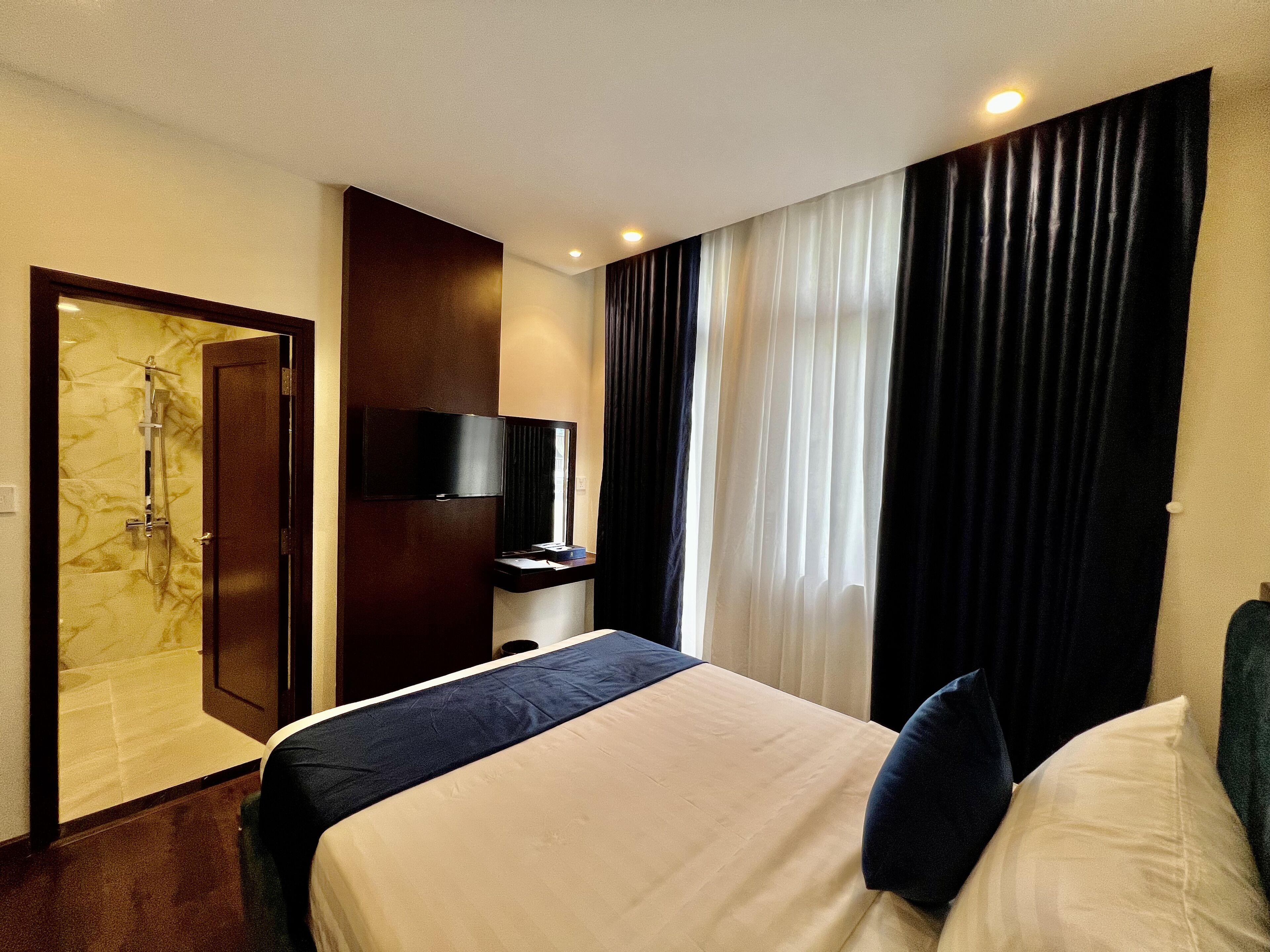 A hotel room with a bed, a TV, a shower, and curtains.