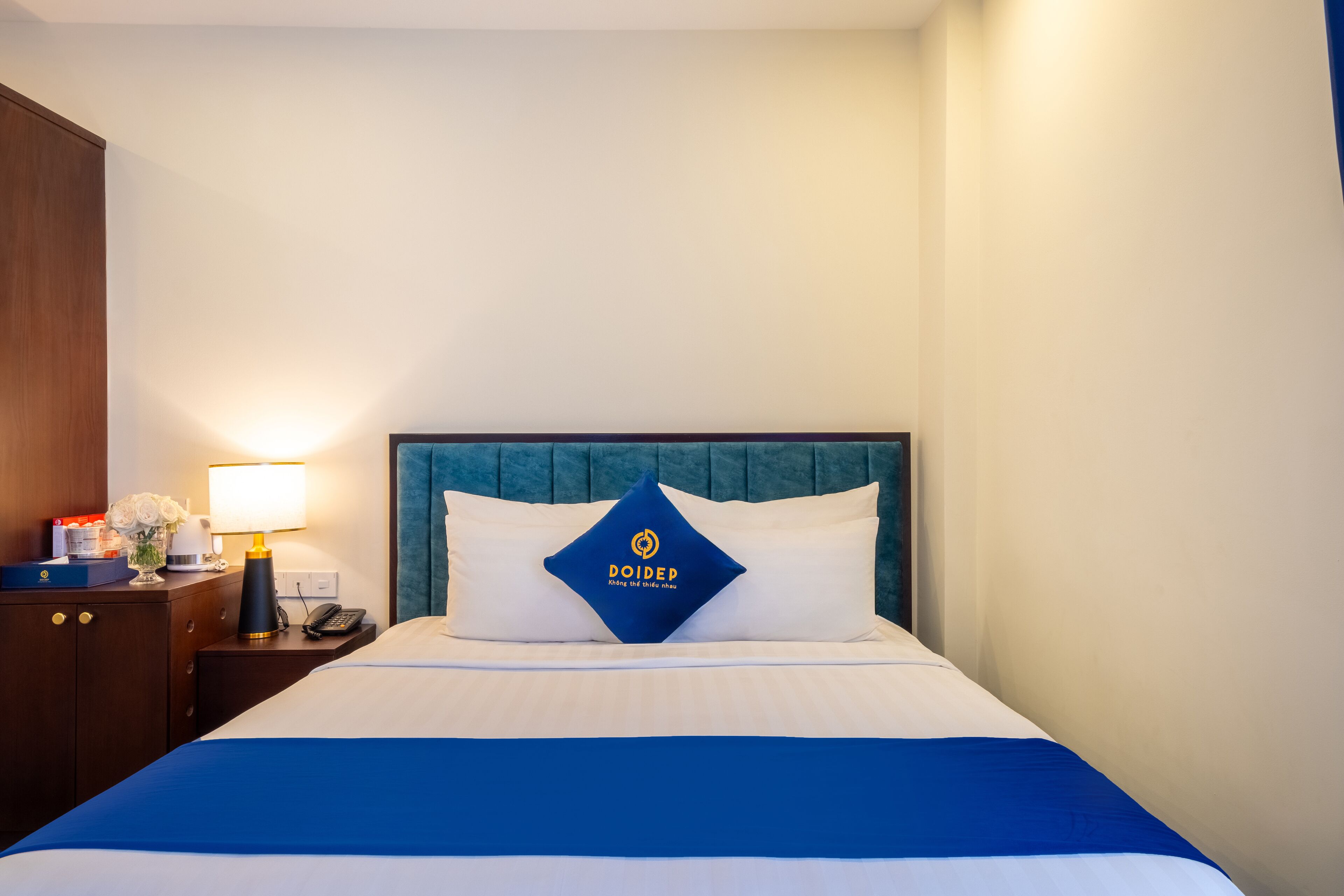 A hotel room with a bed, a nightstand with a lamp, a phone, and a blue and white bedspread.