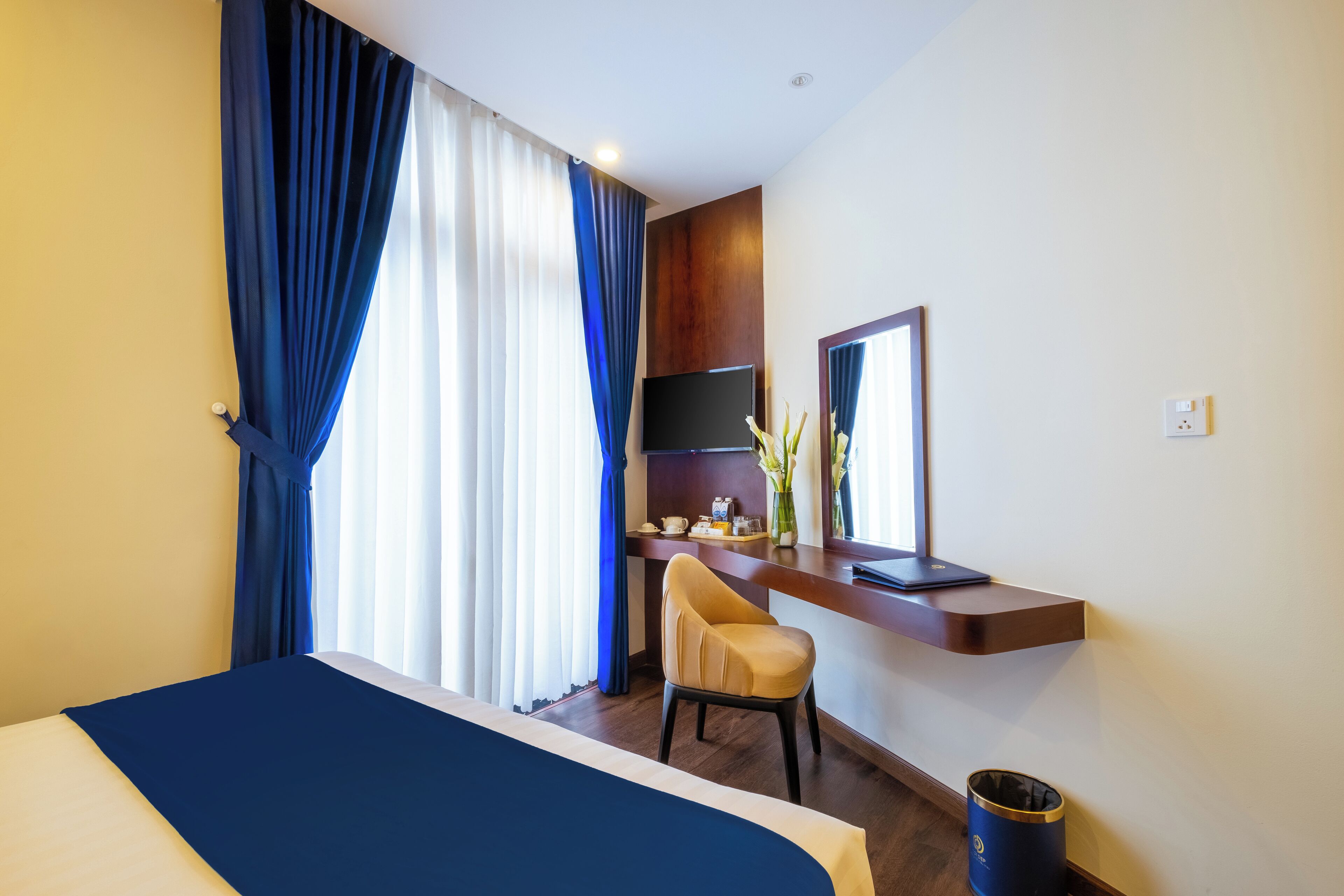 A hotel room with a bed, a desk, a chair, a TV, and a window with curtains.