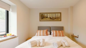 A neatly made bed with two pillows, a framed painting above, and a window with blinds. - Fully Accessible-Disabled Adapted-Hot Tub-Pets (Coughton)