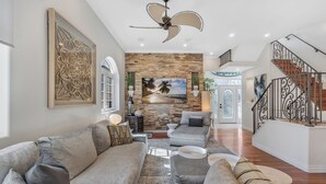 Un salón espacioso con un sofá modular gris, una pared de piedra decorativa y una escalera con barandilla de hierro forjado.