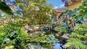 Un jardín tranquilo con un estanque, abundante vegetación y un puente de piedra.