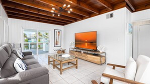 Un soggiorno moderno con un divano grigio, una poltrona bianca, un tavolino in legno e una TV su un mobiletto in legno.