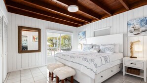 Una camera da letto con un letto grande, travi in legno a soffitto, pareti bianche e vista sull'esterno.