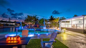 Zona piscina con sedie e un tavolo, un edificio con ampie finestre e un solarium ben illuminato.